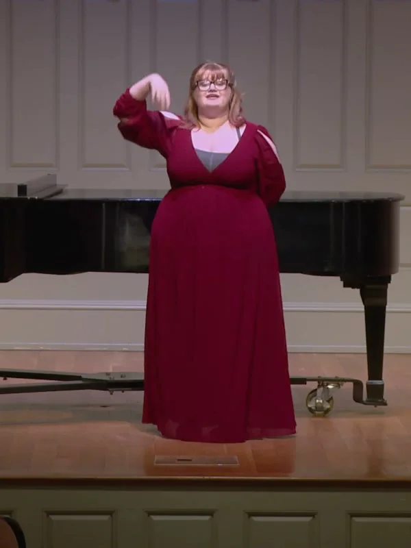 Ophir in a long crimson gown performing in recital beside a grand piano